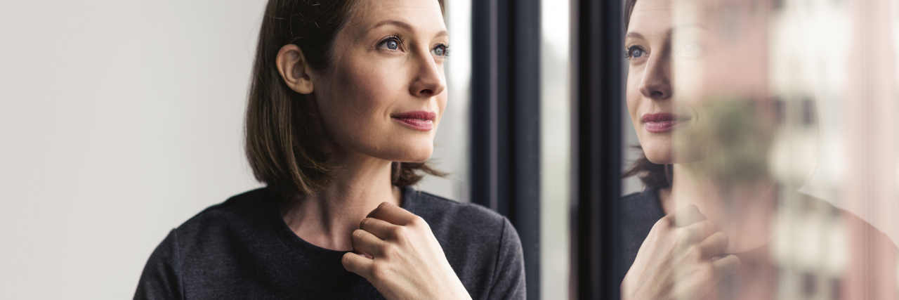 Feeling Seen After Being Diagnosed With a Learning Disability A woman with short brown hair and blue eyes wearing a gray top looks through a window.