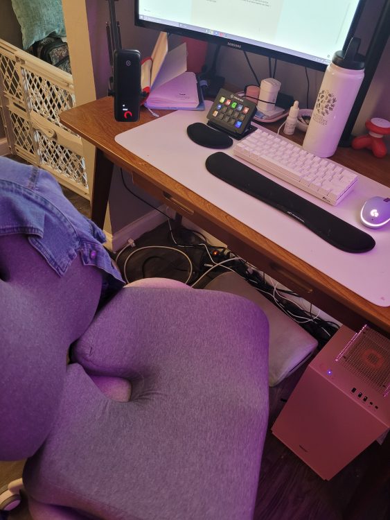 A chair with seat cushions for wrist, butt, and back, a desk, a keyboard, with a purple light emitting.