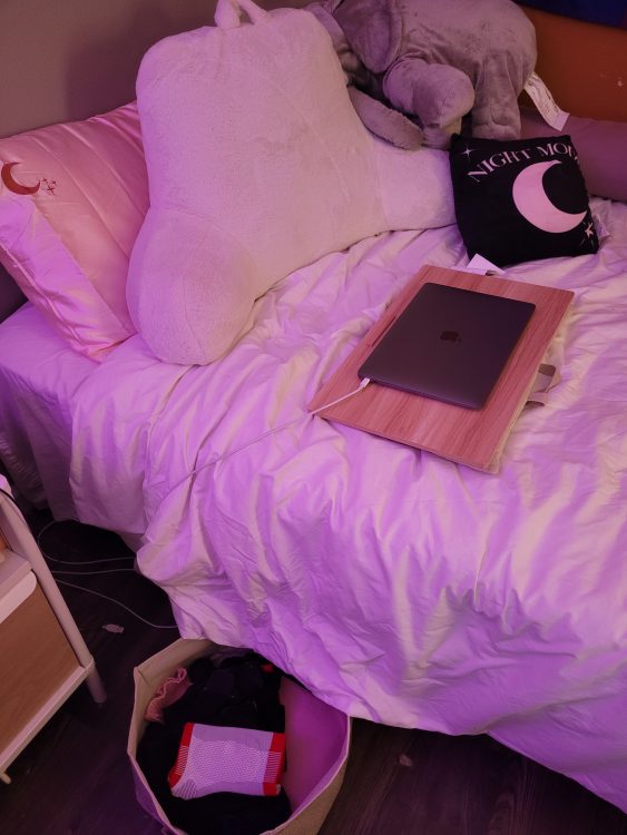A bed with white sheets, a bamboo lap desk, and a computer