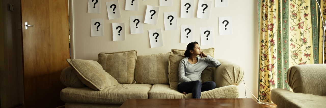 photo of a person sitting on a sofa with question marks stuck to the wall in paper