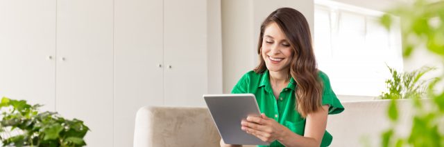 Woman wearing green shirt smiling as she uses a tablet.