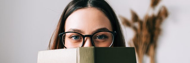 Woman looking over the top of a book.
