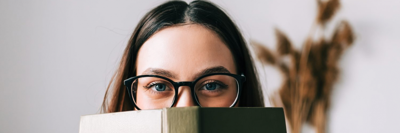 Why I Don't Regret Quitting School for My Mental Health Woman wearing glasses and peeking over the top of a book.