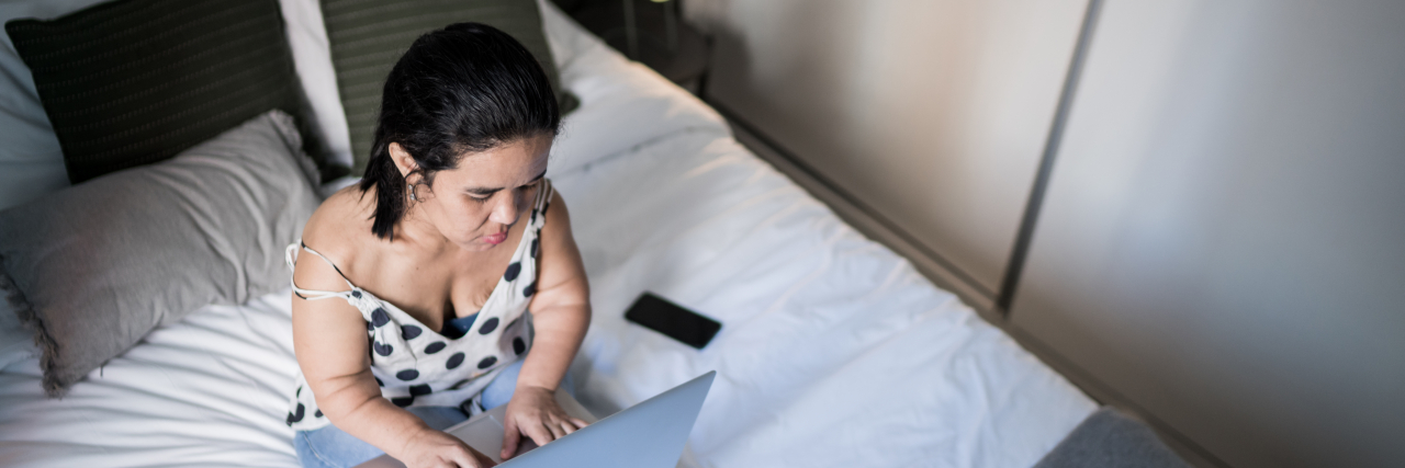 Woman with dwarfism using laptop on bed at home.