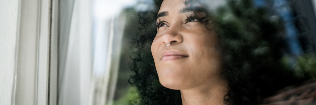 49 Things That Don't Define Your Worth if You Struggle With Confidence Young woman looking through window at home