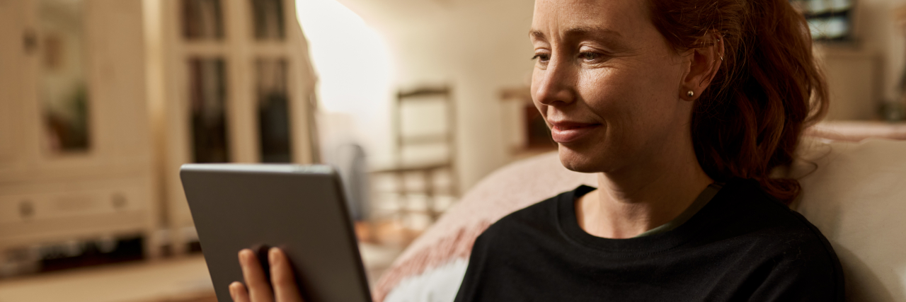 How Pandemic Isolation Allowed Me to Better Understand My Autism Smiling young woman sitting on her bedroom floor reading a tablet.