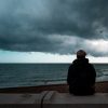 Back of a man sitting alone on the beach as a dark storm approaches