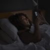 Woman using smart phone while lying in bed.
