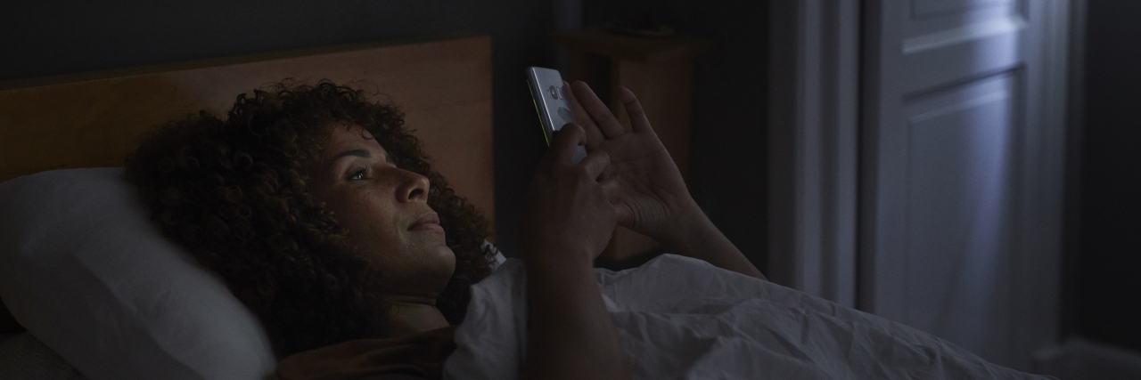 Woman using smart phone while lying in bed.
