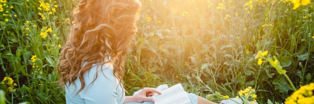 Woman sitting in a flower field reading a spiritual book.
