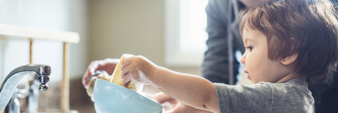Why Childhood Abuse Makes Adulting Hard photo of a toddler learning to wash up dihes with the help of a parent
