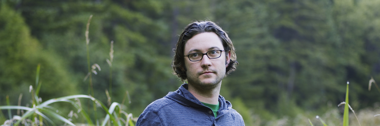 This Common Diagnostic Assessment Tool Is Failing Adults With Suspected Autism. Here's How. A man stands in a field of tall grass at dawn. His hands are in his pockets and he looks listlessly to the side.