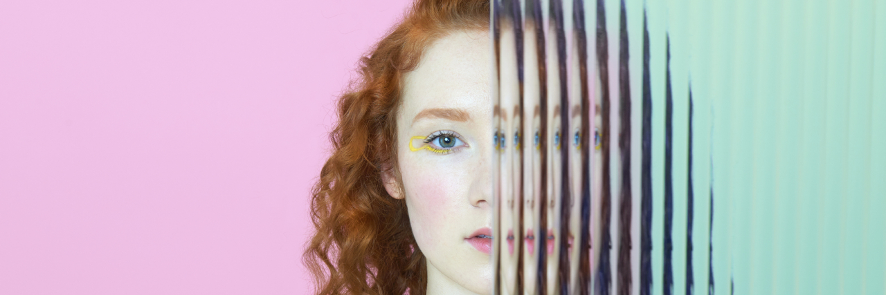 Young woman with curly red hair staring into the camera, half her face being split through glass