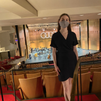 A photo of Carly Fox, a 20 year-old white woman, standing inside at the National Arts Centre of Canada in a deep blue wrap dress.