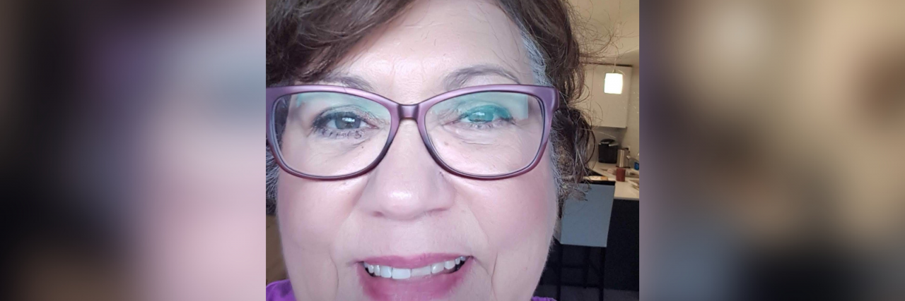 What Helps a Woman in Her Sixties With ADHD A white woman with short brown hair and glasses wearing a purple and white shirt smiles.