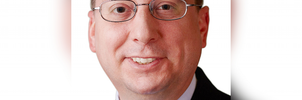 What Helps a Man in His Fifties With Primary Immunodeficiency A white man with brown hair and brown eyes wearing glasses and a black suit with a red tie smiles.