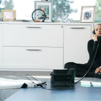 Amanda Seyfried in a black turtleneck sitting against a desk making a phone call