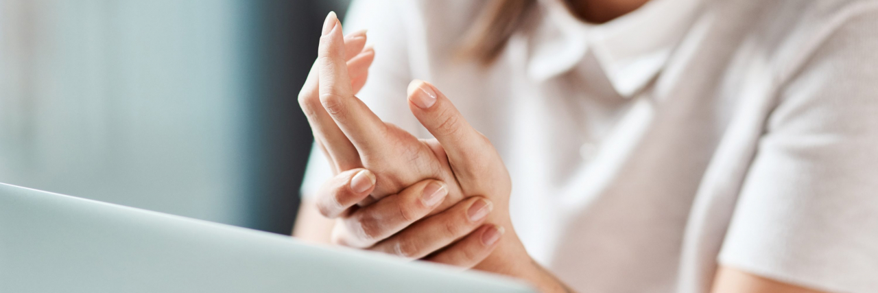 A woman wearing a white short-sleeved blouse and sitting in front of a laptop holds her hand in pain.