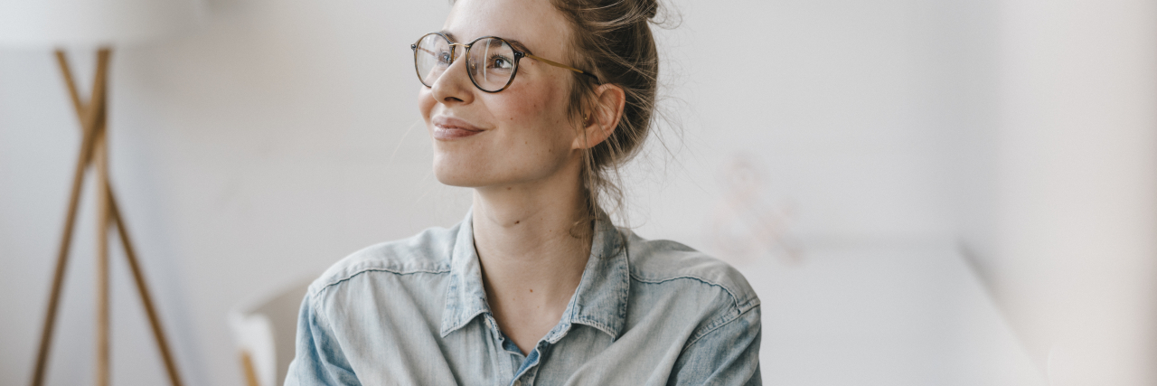 A woman with blonde hair in a bun and a denim shirt crosses her arms with pride.