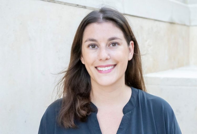 A white woman with brown hair and brown eyes wearing a blue blouse smiles. 