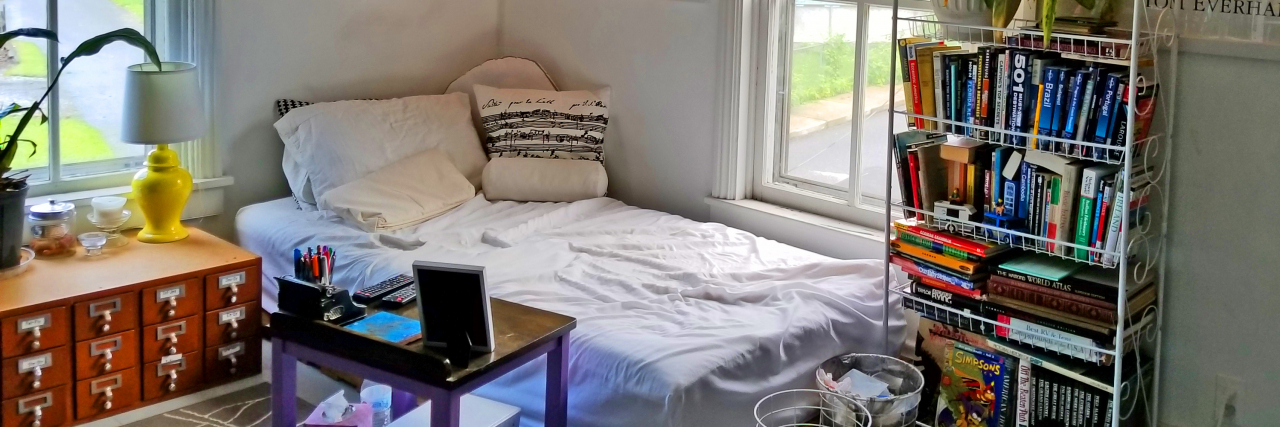 Tips on Making Work From Home Offices Disability-Friendly In a home office there's a bed and a desk near it, a bookshelf with different books and a plant on top. There are christmas lights along the ceiling.