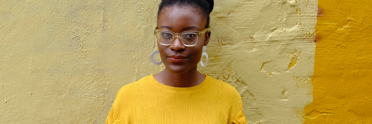 Why the 'Black Girls Don't Get Eating Disorders' Myth is Dangerous photo of a young woman in a yellow sweater standing in front of a yellow painted wall