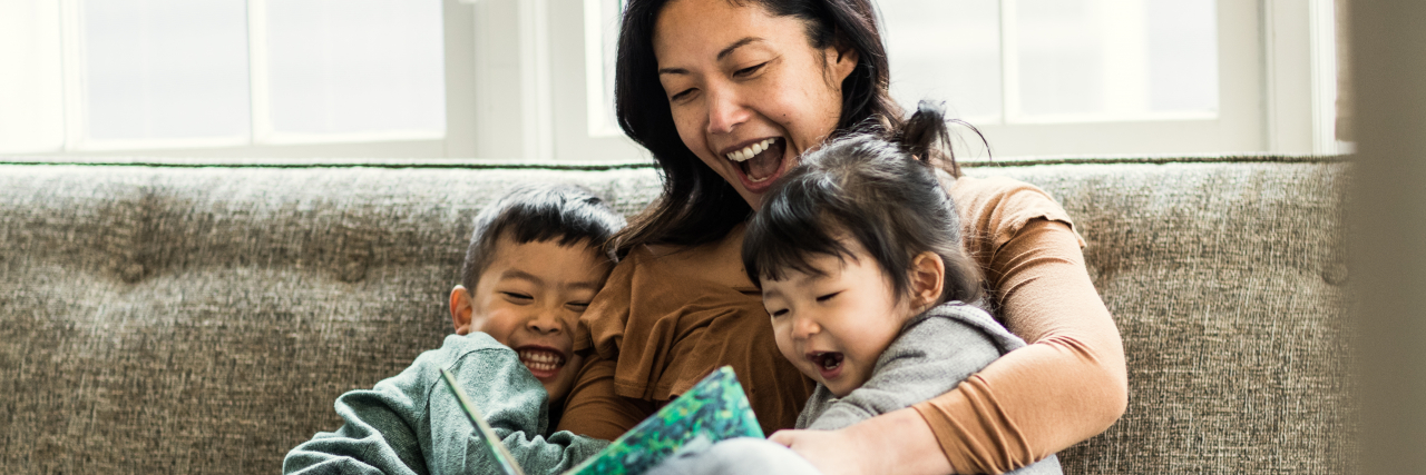 Valuable Lessons for Parents of Multiple Disabled Children A woman hugs two children, a boy and a girl, as she reads to them. All three are smiling.