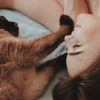 photo of a woman lying down smiling with a cat touching her face