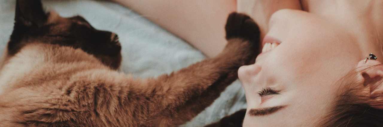 Essential Schizophrenia Coping Skills photo of a woman lying down smiling with a cat touching her face