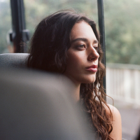 A woman with curly brown hair looks out the window of a bus.