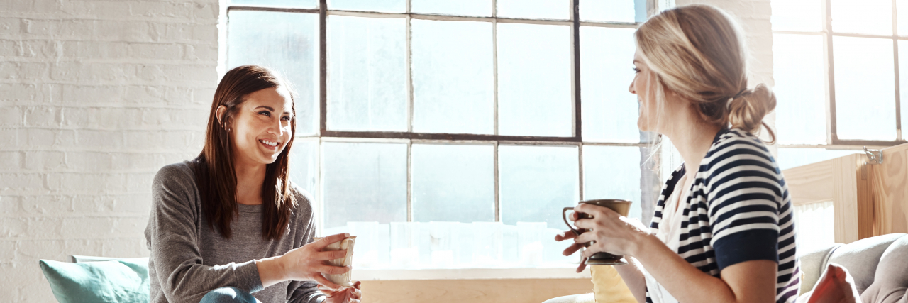 Why You Shouldn't Share Someone's Else's Disability or Illness A brunette woman and a blonde woman chat while sitting down and drinking from ceramic mugs.