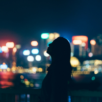 Silhouette of woman looking up towards sky against illuminated and multi-colored cityscape at night