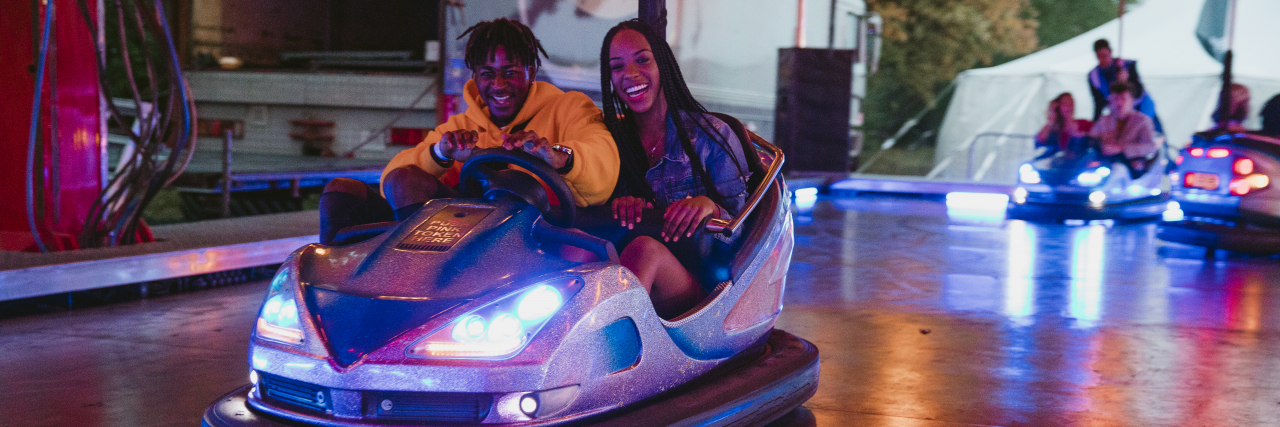 Young couple are having fun racing around on bumper cars at a funfair.