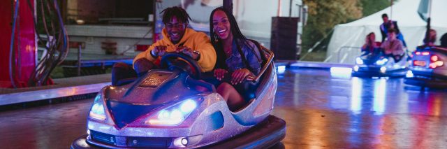 Young couple are having fun racing around on bumper cars at a funfair.