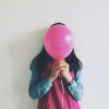 Woman Covering Face With Balloon Standing Against Wall