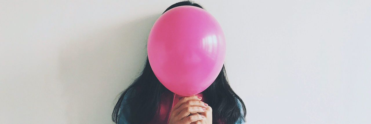 Woman Covering Face With Balloon Standing Against Wall