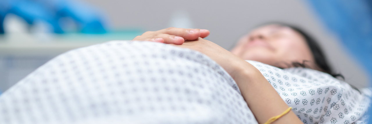 We Need to Talk About the Emotional and Physical Trauma of a C-Section Pregnant woman wearing hospital gown and laying on operating table in preparation for surgery