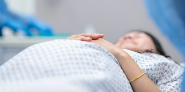 Pregnant woman wearing hospital gown and laying on operating table in preparation for surgery