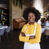 Portrait of positive African american young woman working professional confectioner in own coffee shop, looking at camera with toothy smile.