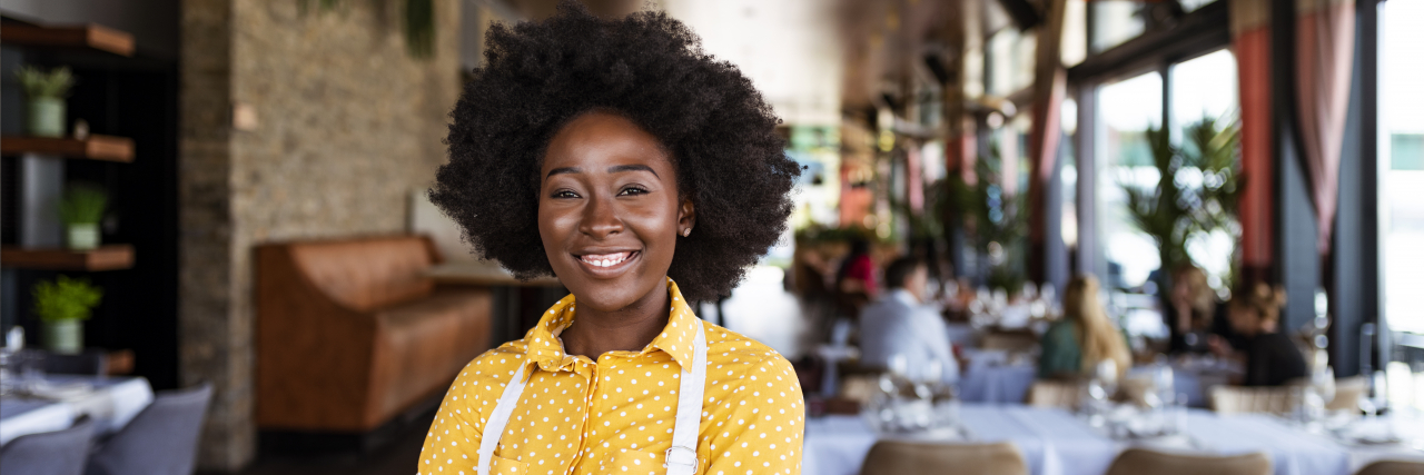 Portrait of positive African american young woman working professional confectioner in own coffee shop, looking at camera with toothy smile.
