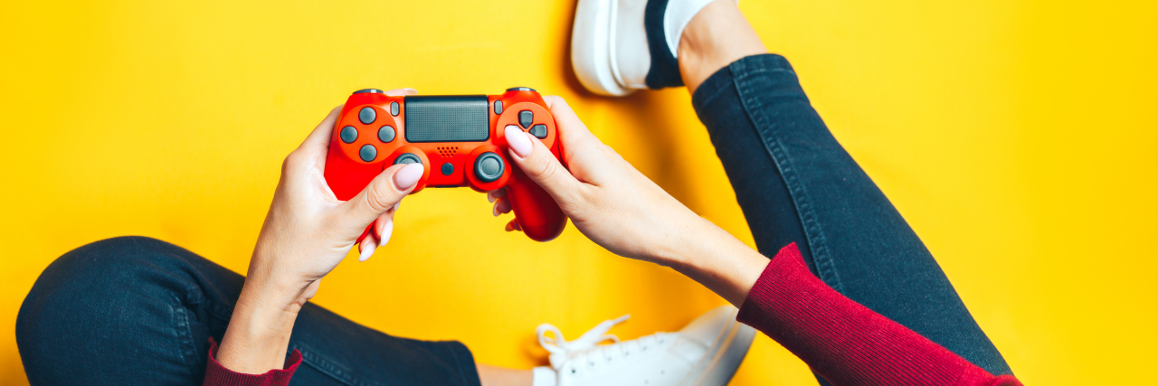 Young thin woman playing with red gamepad, sitting on yellow background. flat lay.