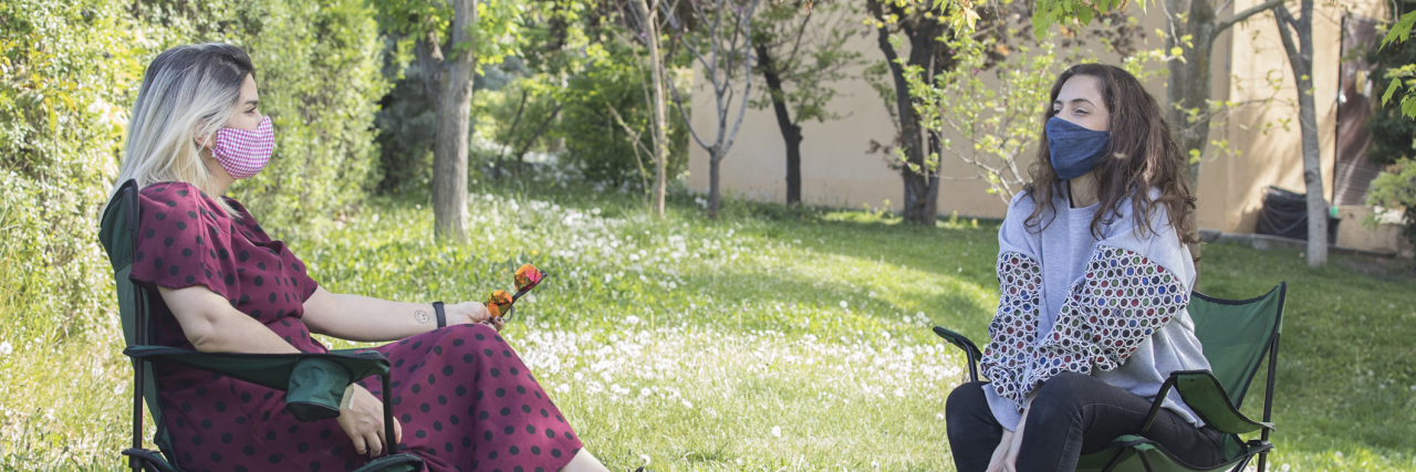 two women sitting outdoors with home made face masks.