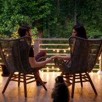 A couple sit in chairs and hold hands on a home patio.