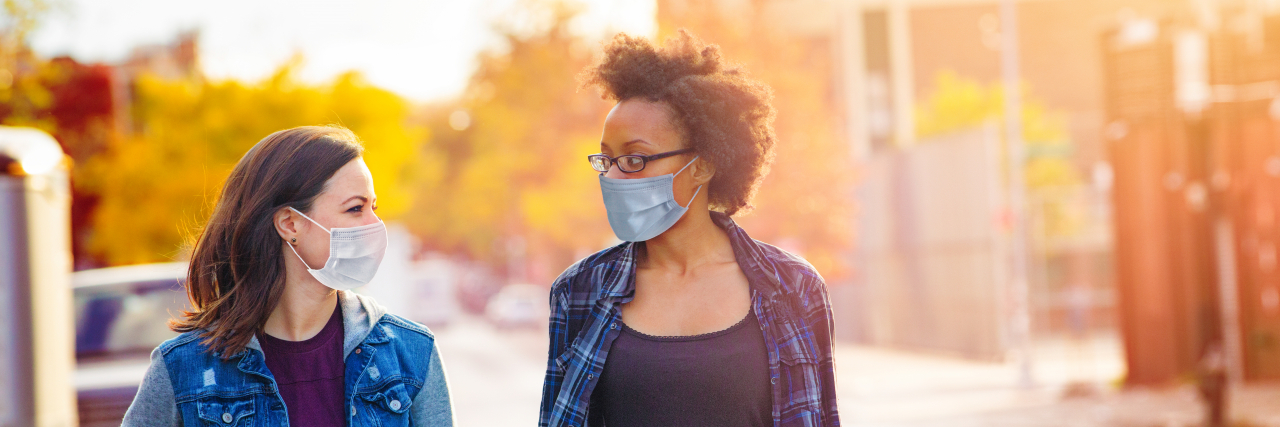 Two female friends walking down a Brooklyn alley wearing face masks.
