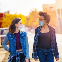 Two female friends walking down a Brooklyn alley wearing face masks.