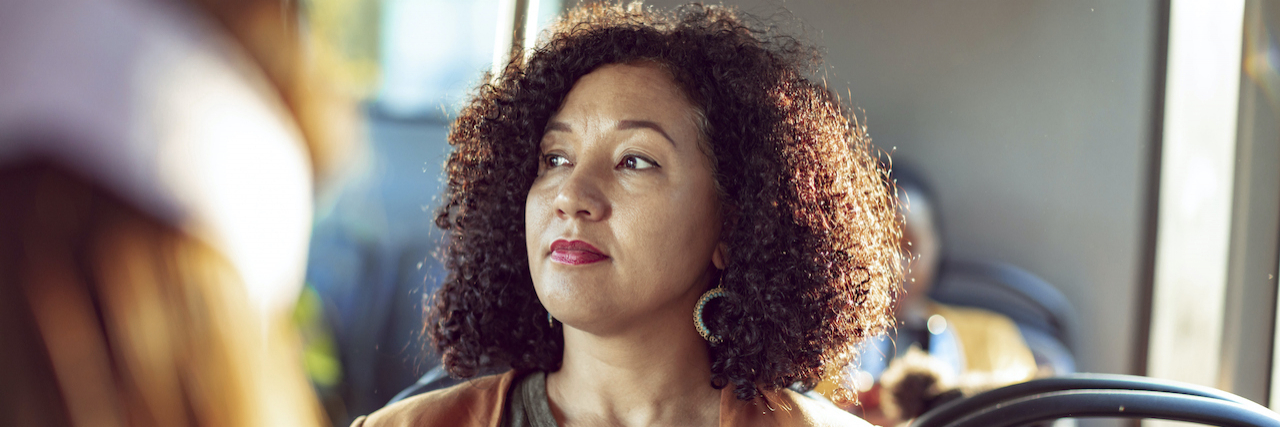 How Limiting Access to Pharmacies Harms Chronic Pain Patients Woman of color sitting on a bus, looking out the window with a neutral expression