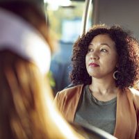 Woman of color sitting on a bus, looking out the window with a neutral expression