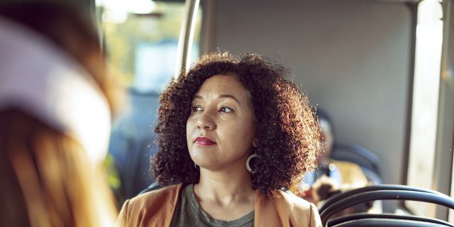 Woman of color sitting on a bus, looking out the window with a neutral expression