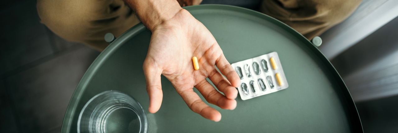 People Share Real Experiences Taking Lithium for Bipolar Disorder photo of a man's hand holding a pill with pill packet and water on the table