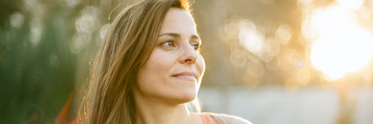Finding Independence After a Mental Health Crisis Woman's portrait at sunset looking to the side, with soft filtered light in the trees behind her